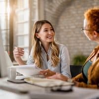 smiling creative businesswoman going through paperwork talking her female colleague office 00